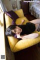 A woman laying on a yellow couch in a bedroom.