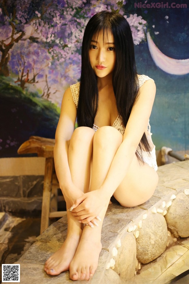 A woman sitting on a stone bench in front of a painting.