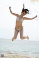 A woman in a bikini jumping in the air on the beach.