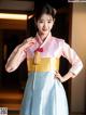 A woman in a pink and blue hanbok poses for a picture.